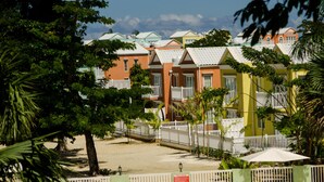 A swimming pool with lounge chairs, a white fence, and colorful buildings in the background. - Tropics at Little Bay Country Club (Negril)