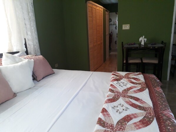 A neatly made bed with a white and patterned bedspread, a wooden headboard, and a small table with chairs in the background.