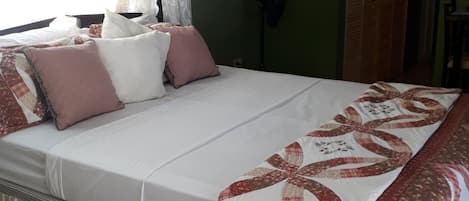 Une chambre à coucher avec un lit, des oreillers, une couette, une fenêtre avec des rideaux et une porte.