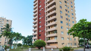 A multi-story hotel with a red and beige facade, balconies, and a parking area with palm trees. - Deluxe Turtle Towers Apartments (Ocho Rios)