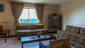 A living room with a sofa, a coffee table, a TV, and a bookshelf. - Deluxe Turtle Towers Apartments (Ocho Rios)