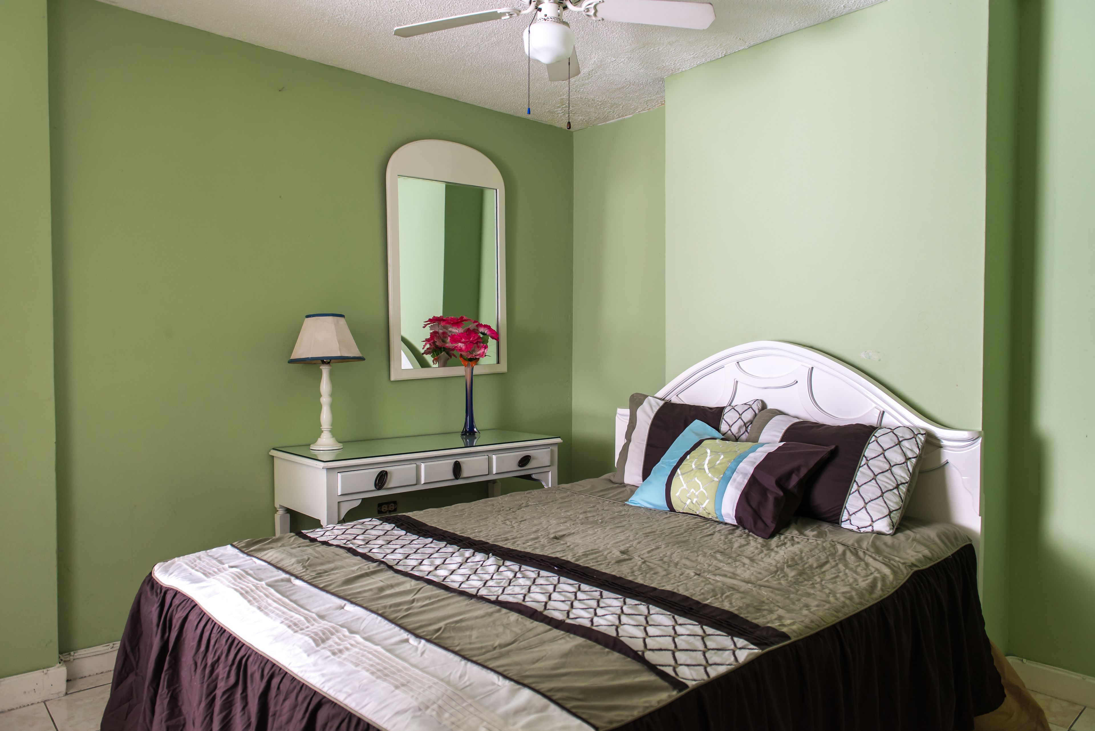 A bedroom with a bed, a dresser, a mirror, and a ceiling fan.