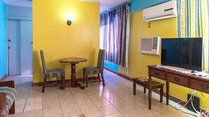 A room with yellow walls, a dining table with chairs, a TV, and an air conditioning unit. - Deluxe Turtle Towers Apartments (Ocho Rios)