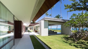 Ein modernes Haus mit überdachter Terrasse, Rasen und Blick auf das Meer.