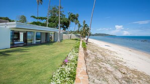 Ein Strandgrundstück mit einem modernen Haus, einem gepflegten Rasen und einem Steinweg, der zum Strand führt.