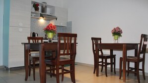 A modern kitchen with wooden cabinets, a dining table with chairs, and two potted plants with flowers. - Harmony Rooms (Catania)