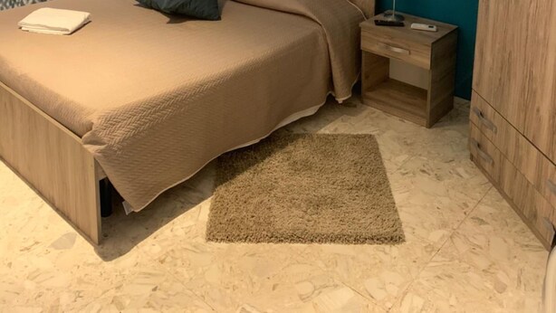 A bedroom with a bed, nightstands, a wooden wardrobe, a cityscape painting, and patterned curtains. - Harmony Rooms (Catania)