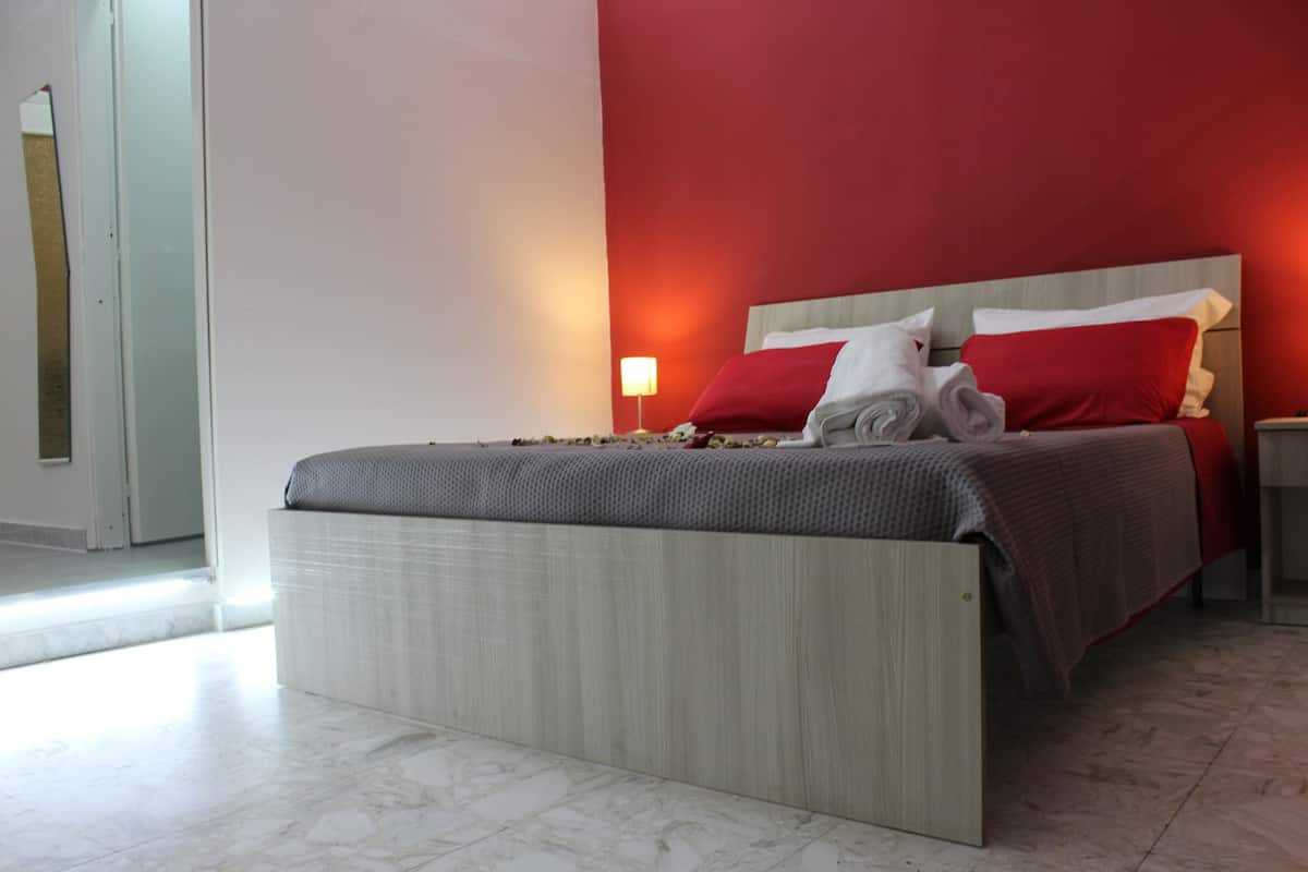 A modern hotel room with a large bed, red accent walls, and a marble floor.