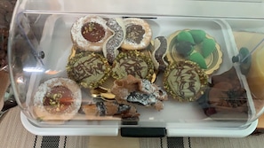 A clear plastic container with various pastries and desserts, some topped with nuts and others with chocolate drizzle. - Harmony Rooms (Catania)