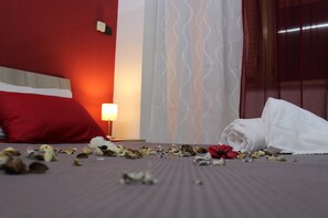 A hotel room with a bed, a red pillow, a white towel, and scattered flower petals. - Harmony Rooms (Catania)