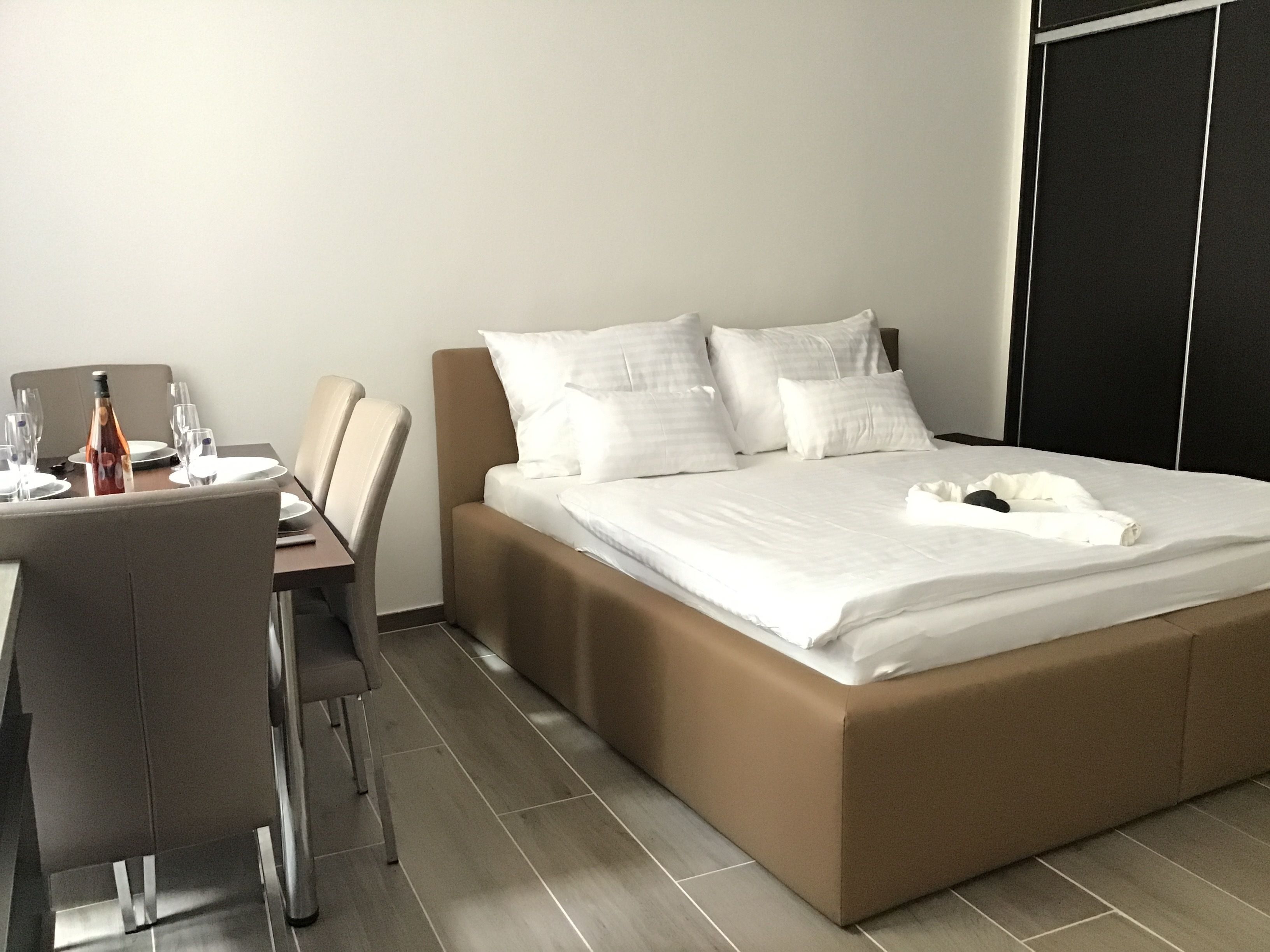 A modern hotel room with a bed, a dining table with chairs, and a wine bottle.