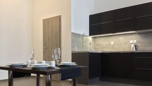 A modern kitchen with dark cabinetry, a built-in oven, and a dining area with a table set for two. - Euro Apartments Lidická 39 Brno (Brno)