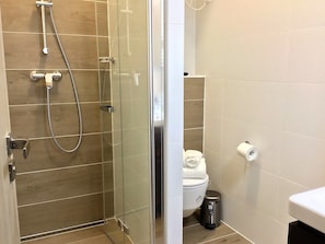 Een moderne badkamer met een douchecabine van glas, een toilet en een prullenbak.