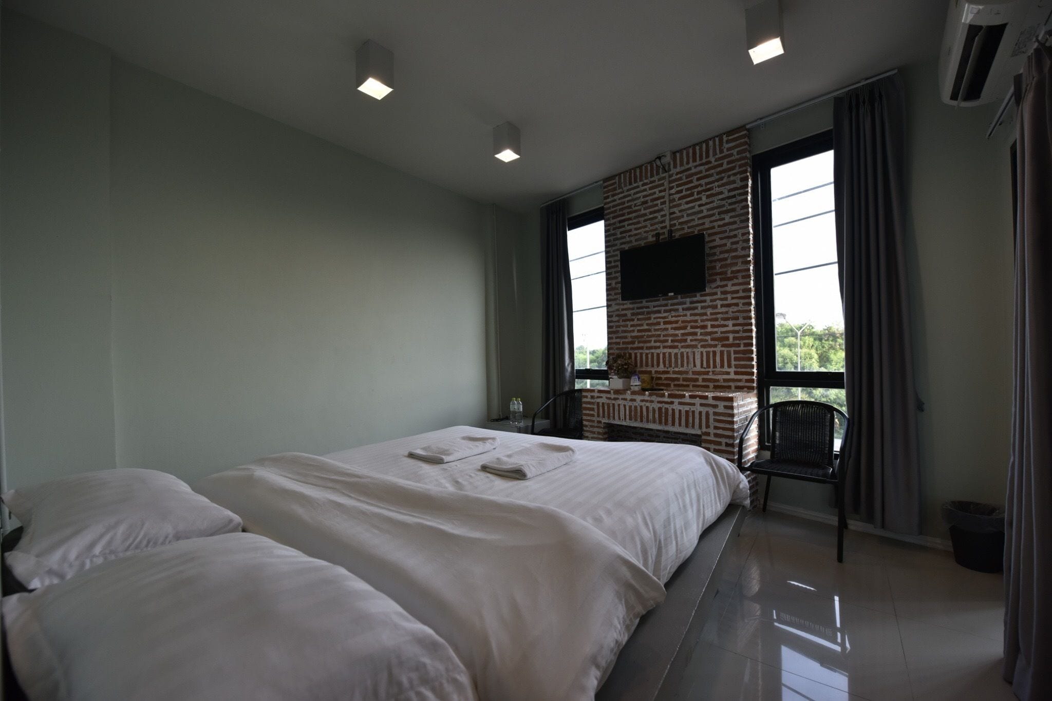 A bedroom with a large bed, a brick fireplace, and a TV mounted on the wall.