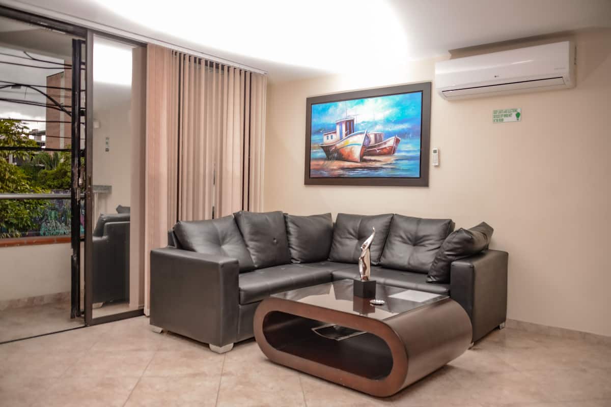 A modern living room with a sectional sofa, a glass coffee table, and a painting of boats on the wall.