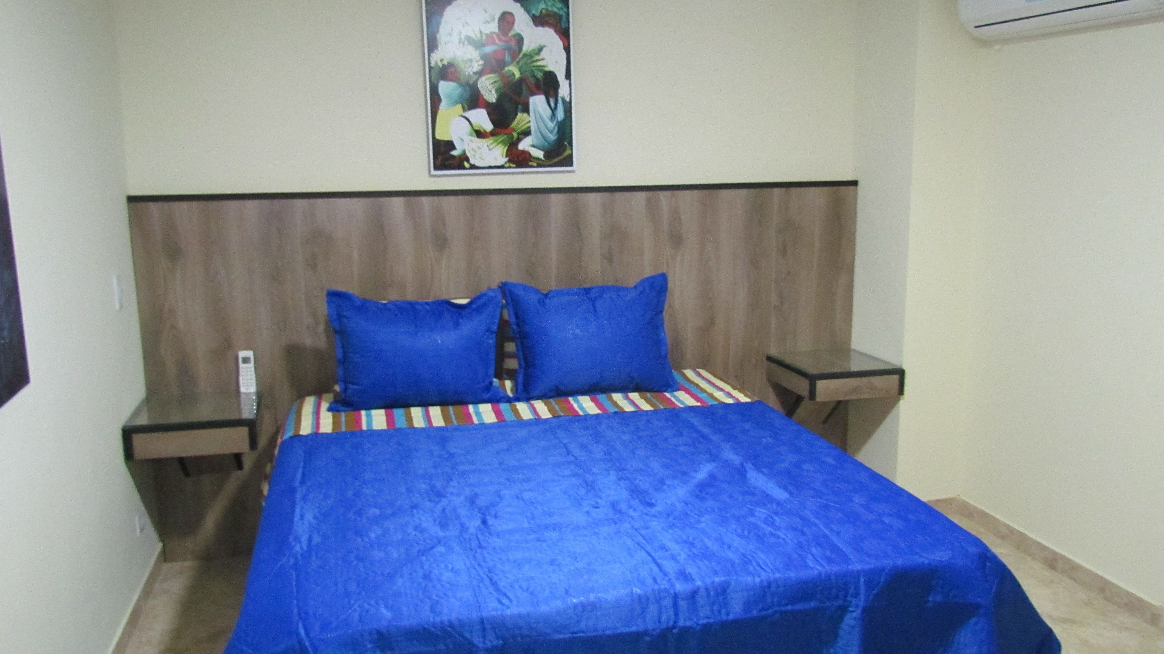 A bed with a blue bedspread and two blue pillows, a wooden headboard, and a small bedside table with a lamp.
