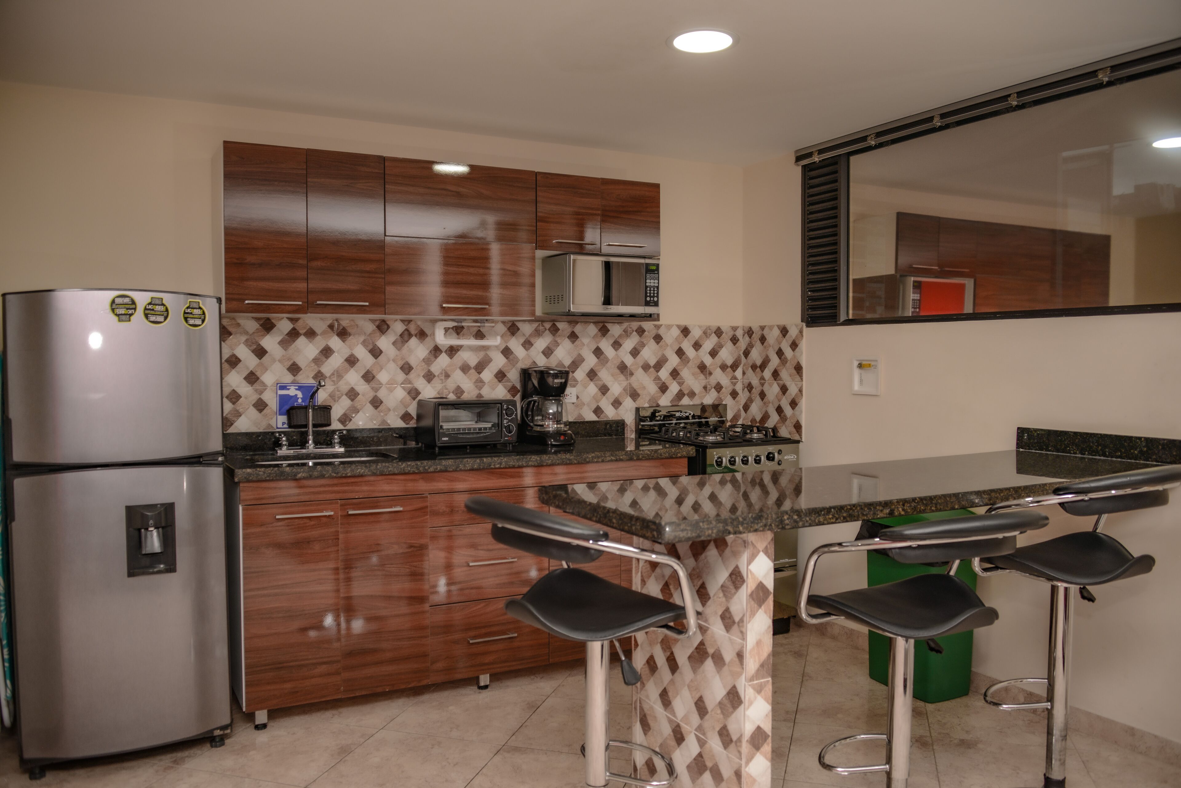 Cucina con mobili in legno, frigorifero in acciaio inossidabile, forno a microonde, piano cottura a gas e zona bar con sgabelli.