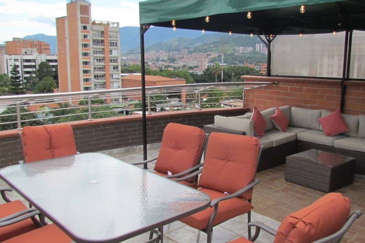 An outdoor patio with a glass table, orange chairs, and a sofa with red cushions.