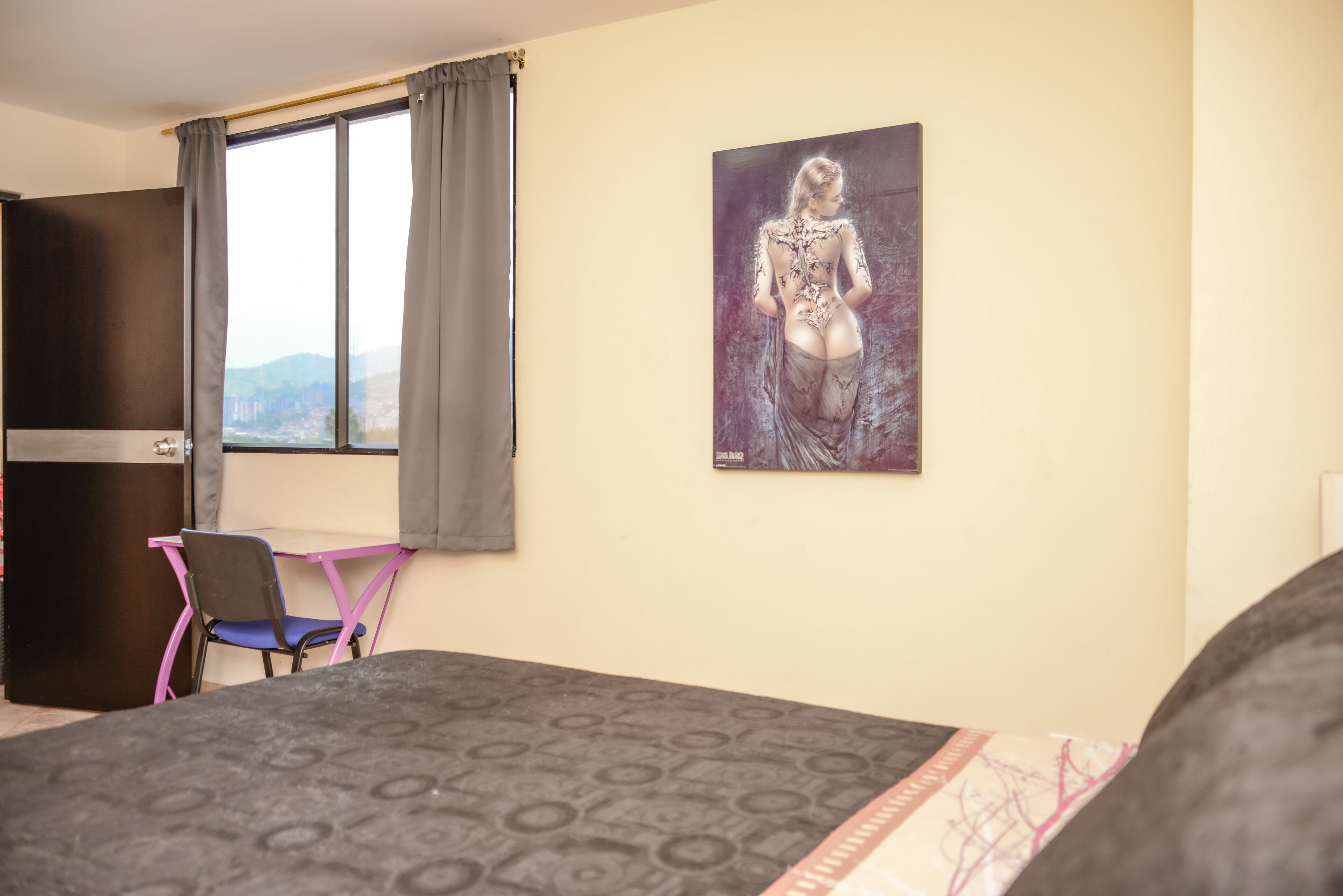 A hotel room with a bed, a desk, a chair, and a large window with curtains.