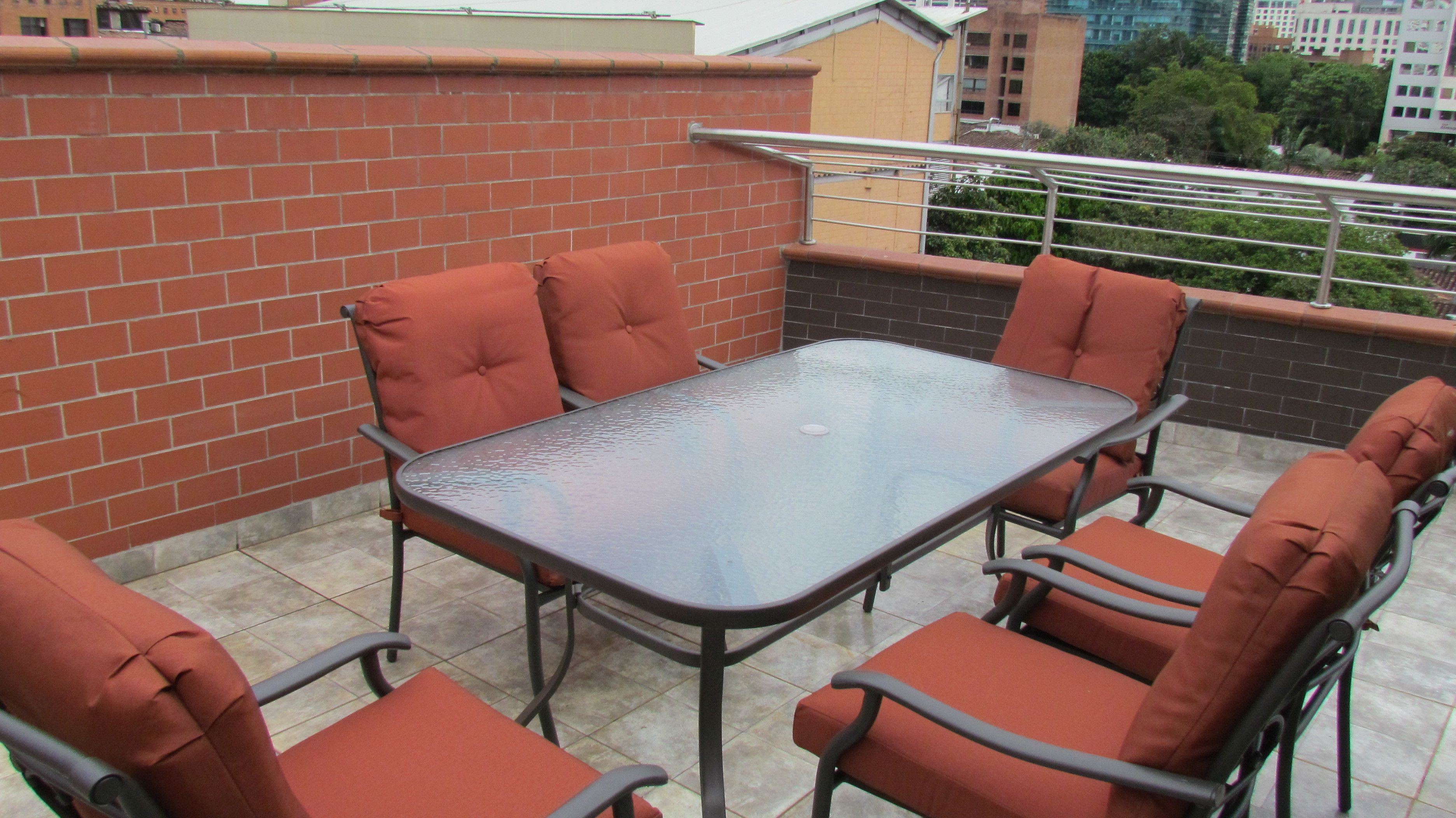 Un patio en la azotea con una mesa de vidrio y sillas con cojines naranja.