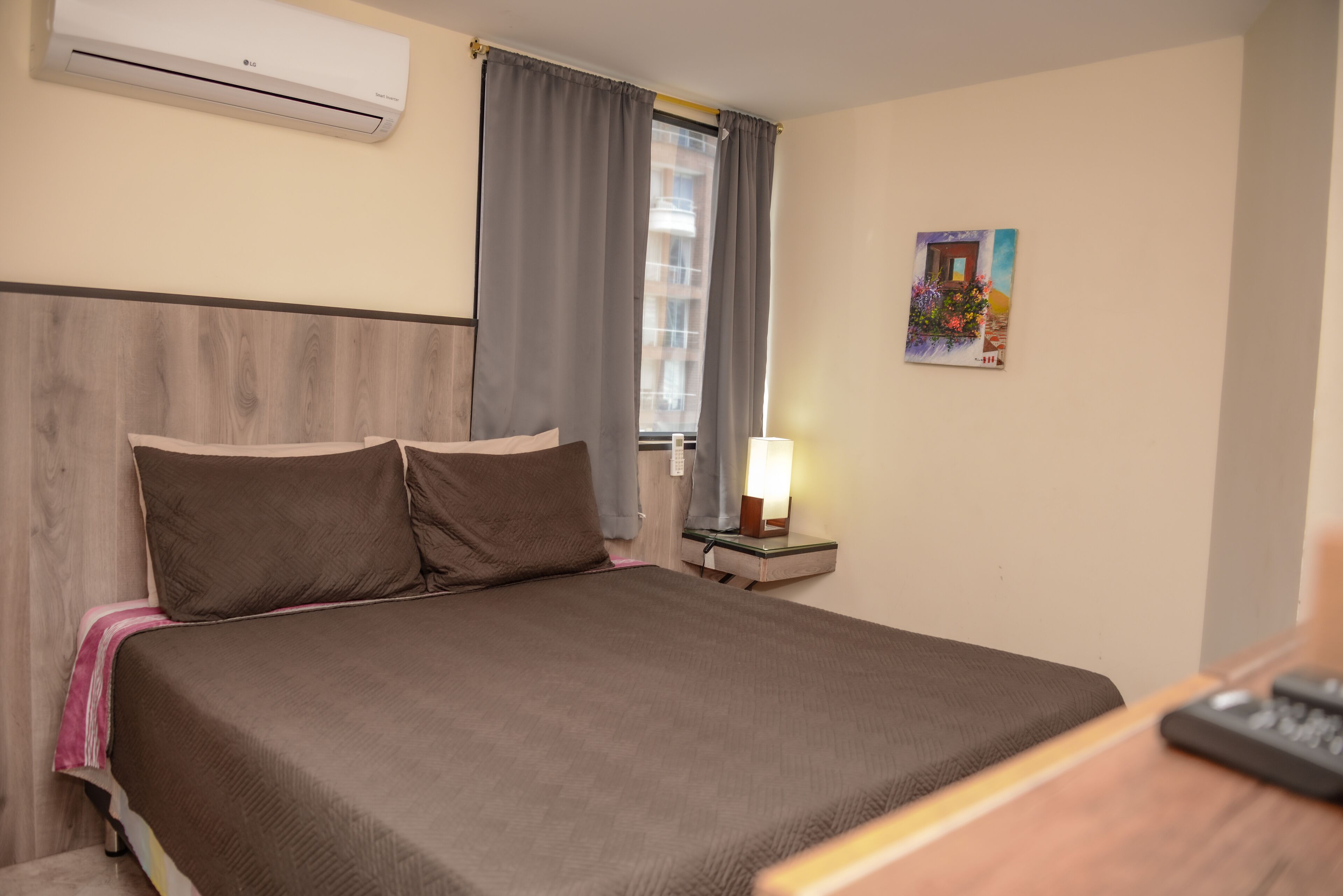 Habitación de hotel con cama, mesita de noche con lámpara, aire acondicionado y ventana con cortinas.