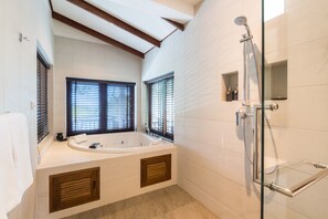 A modern bathroom with a freestanding bathtub, a glass-enclosed shower, and a window with blinds.