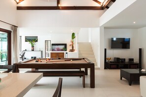 Amplia sala de estar con mesa de billar, televisor y escalera que conduce a un nivel superior.