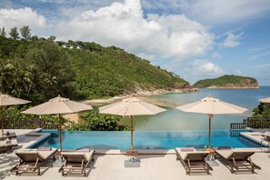 A pool area with lounge chairs and umbrellas, overlooking a beach and a mountainous landscape.