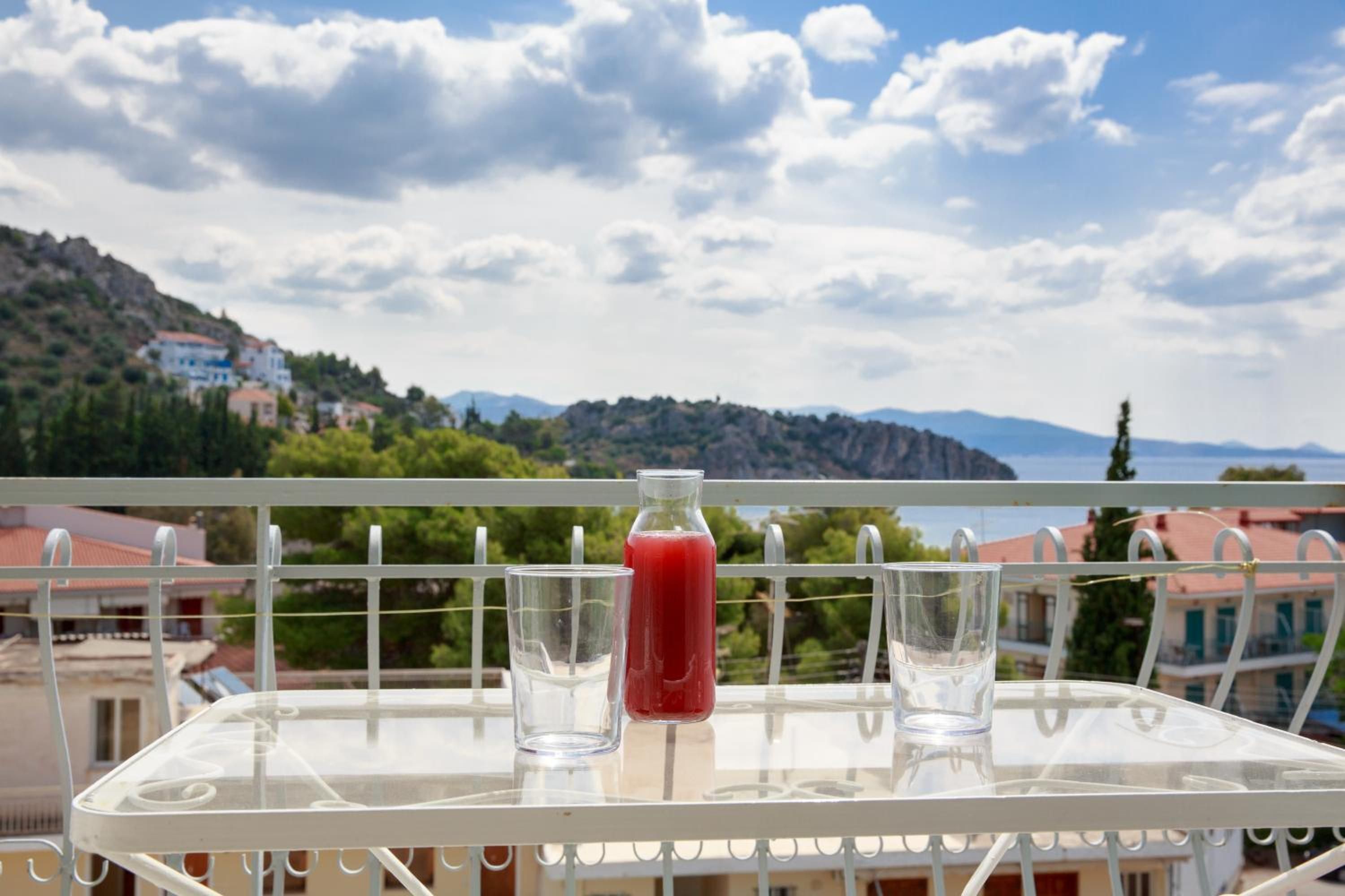 A balcony with a table, a glass of red drink, and a clear view of a mountainous landscape.