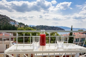 A balcony with a table, a glass of red drink, and a clear view of a mountainous landscape. - Psili Ammos (Nafplio)