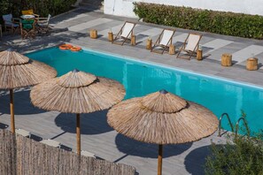 Una piscina con sillones de madera y sombrillas de paja.