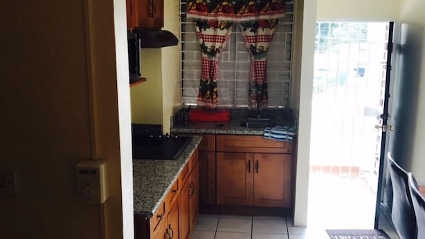 Una cocina con armarios de madera, encimera negra y ventana con cortinas estampadas.