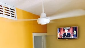 Una sala de estar con un sofá, un televisor montado en la pared y una mesita con un florero.