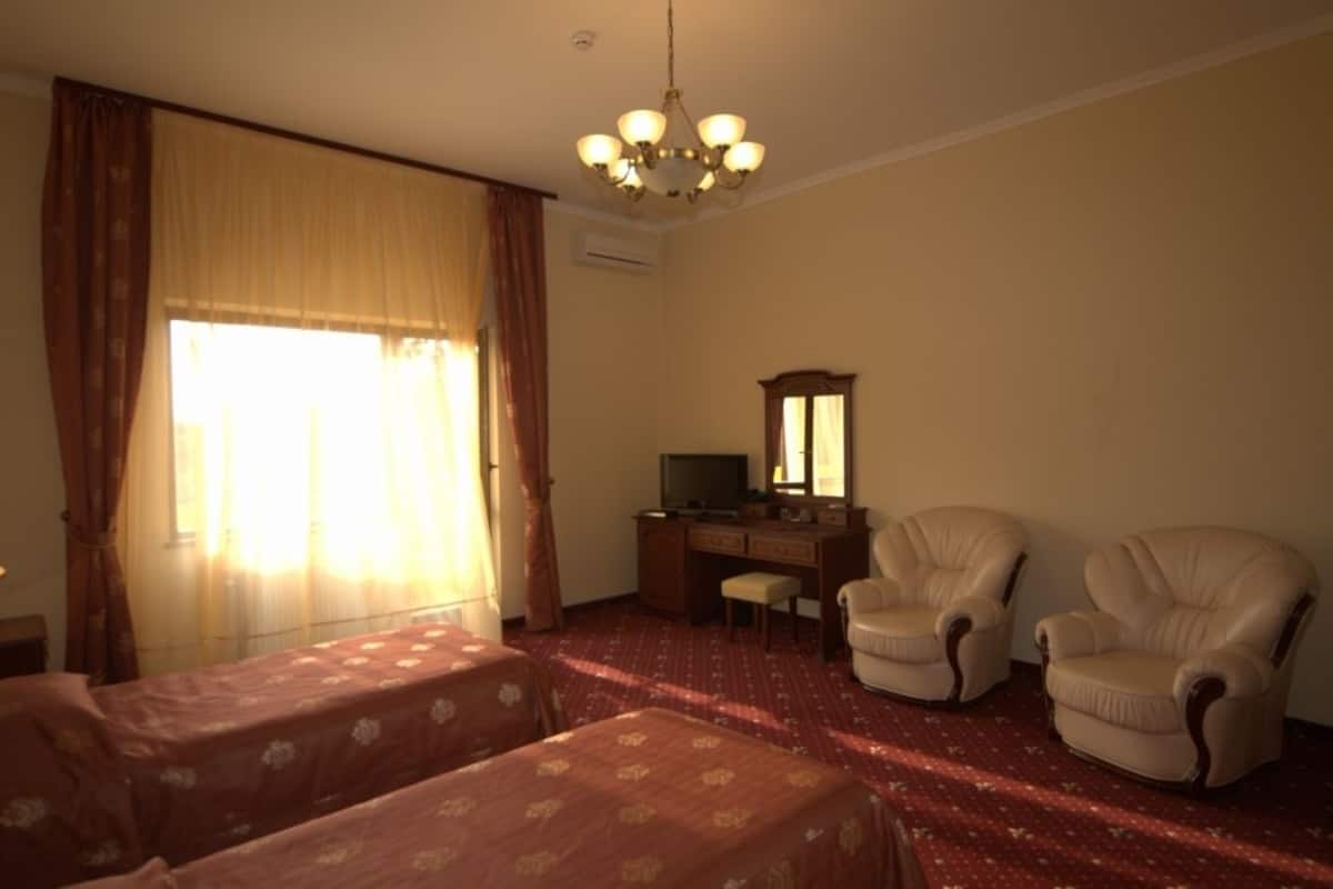 Habitación de hotel con dos camas, un escritorio con televisor, dos sillones y un candelabro.