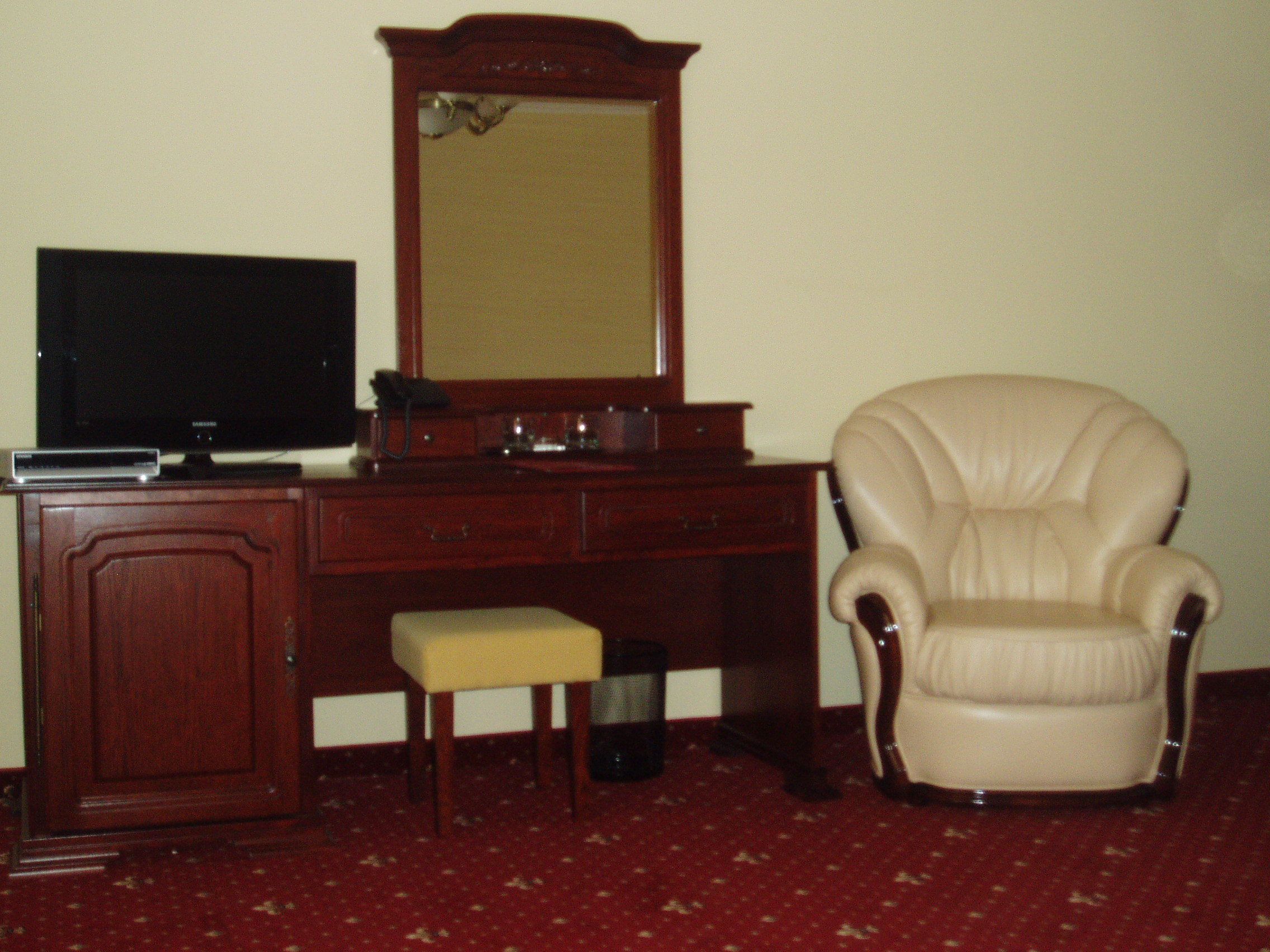 A room with a wooden desk, a television, a mirror, a chair, and a small stool.