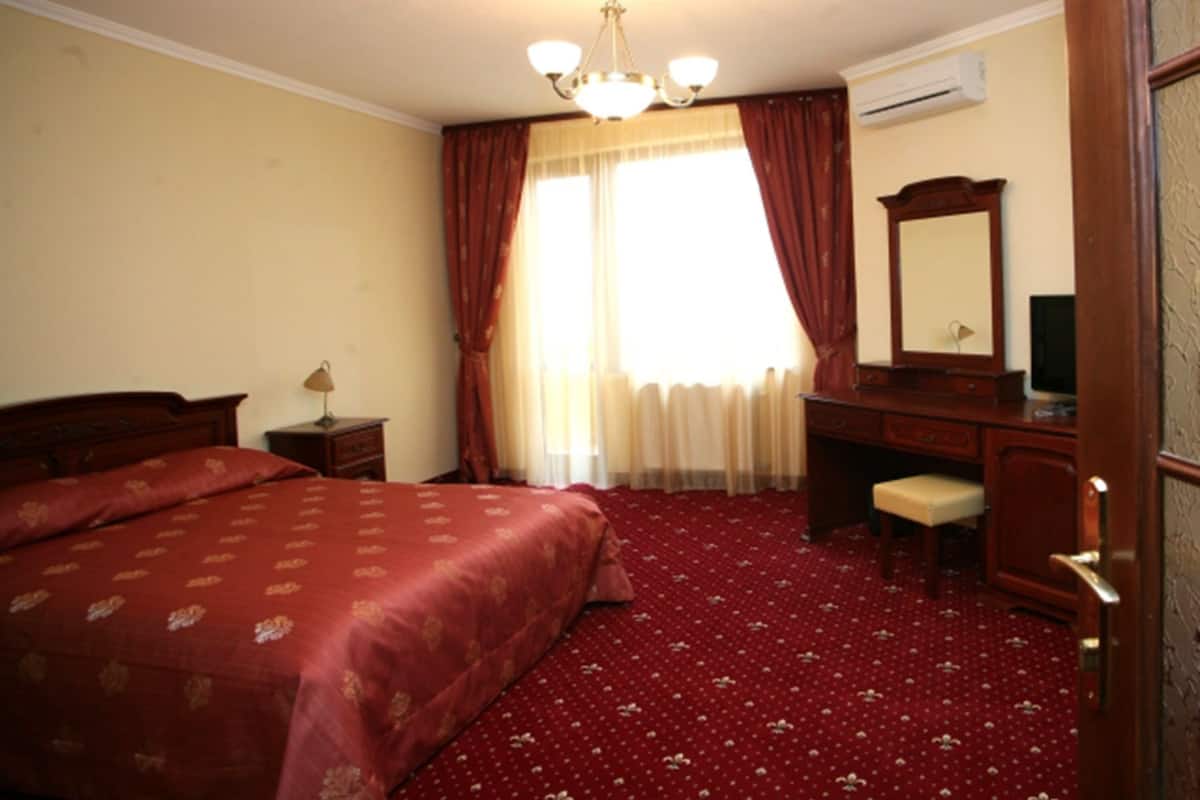 Una habitación de hotel con una cama grande, un escritorio, una silla, un espejo y una ventana con cortinas.