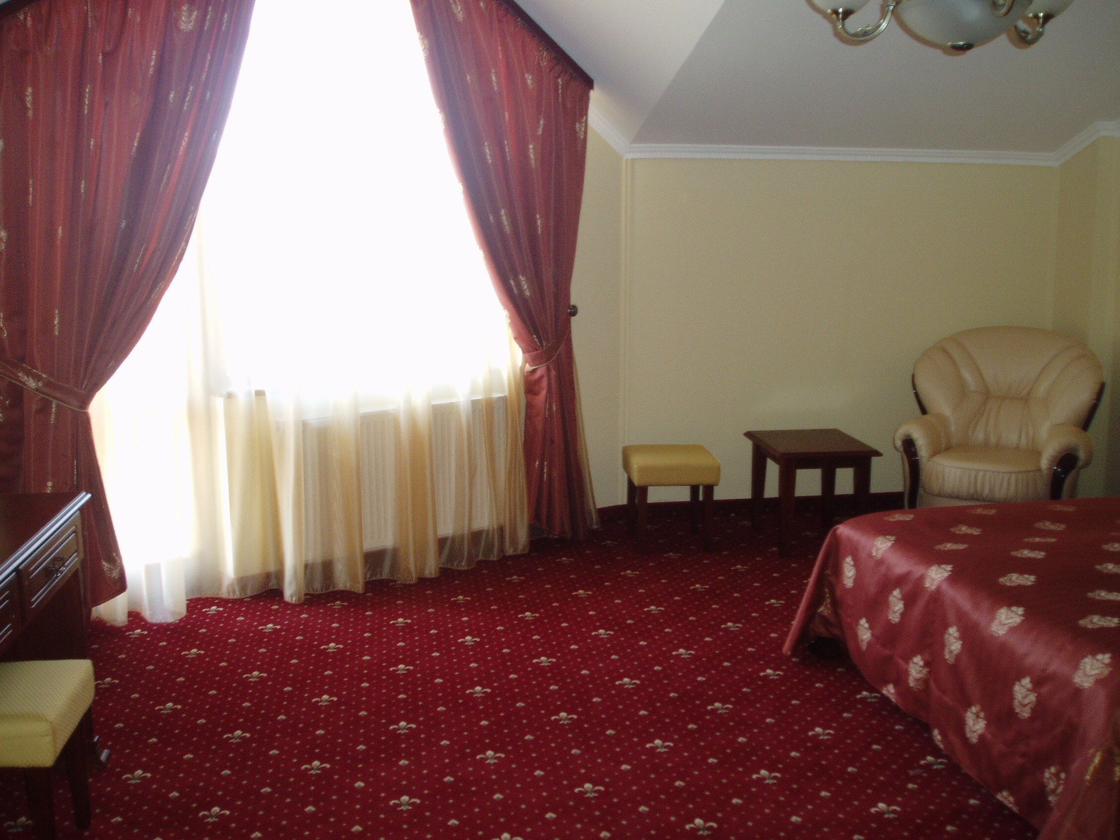 Une chambre d’hôtel avec un tapis rouge, un lit, une chaise, une petite table et un bureau avec une chaise.