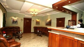 A hotel lobby with a reception desk, leather sofas, a chandelier, and framed artwork on the walls.