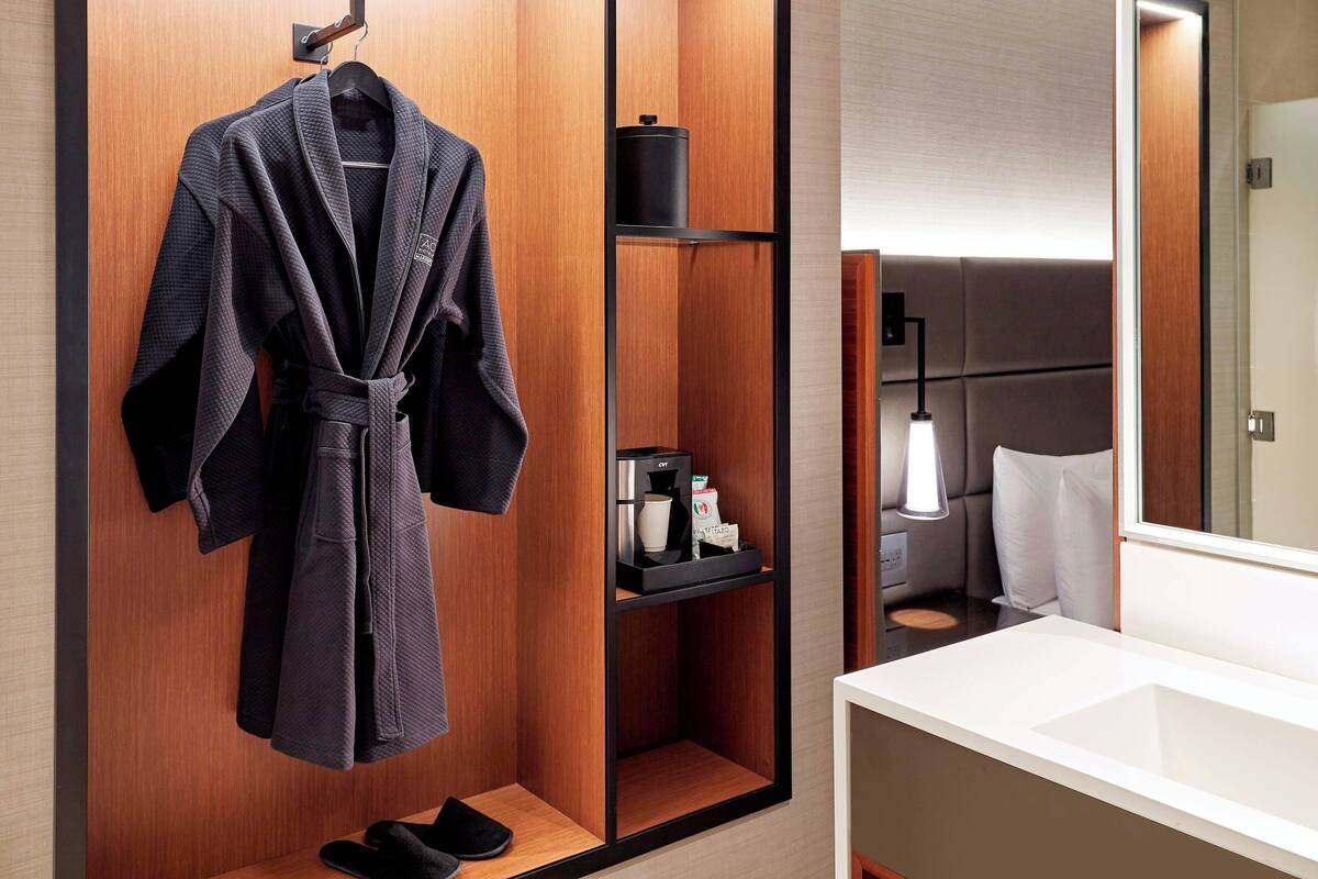 A modern bathroom with a wooden vanity, a robe hanging on a rack, a shelf with toiletries, and a mirror.