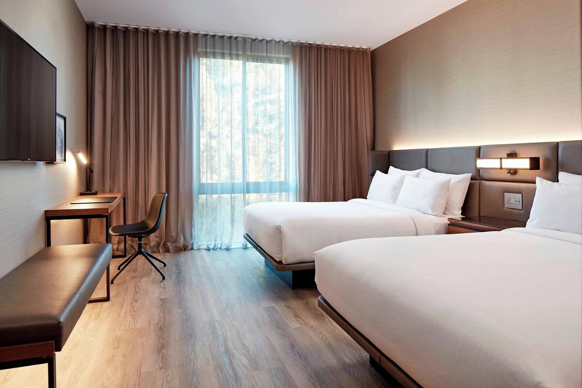 A hotel room with two beds, a desk, a chair, and a TV.