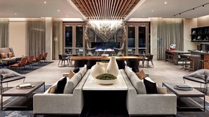 A modern hotel lobby with a central seating area, a fireplace, and a bar.