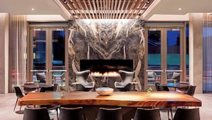 A modern dining area with a large wooden table, black chairs, and a central fireplace.