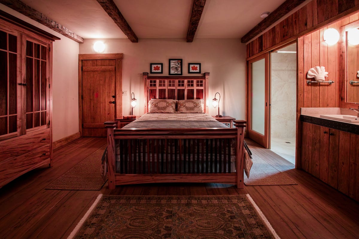 A wooden bedroom with a bed, bedside lamps, and a wooden wardrobe.