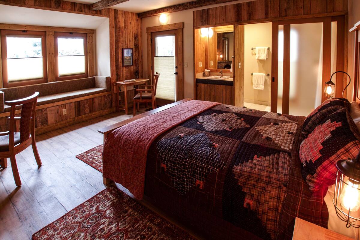 A cozy bedroom with a large bed, a wooden desk, a chair, and a window.