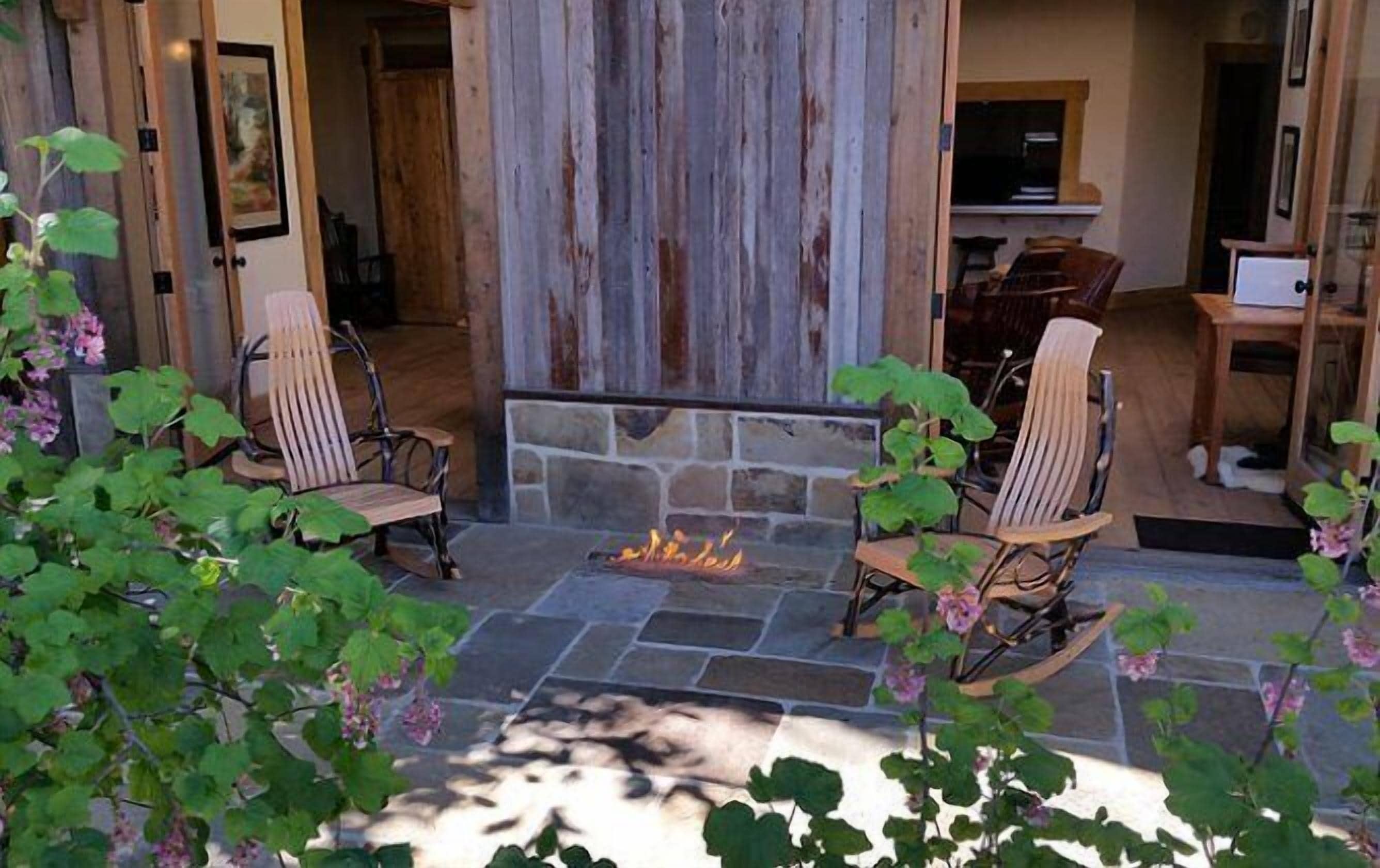 A stone fireplace with two rocking chairs facing it, surrounded by greenery.