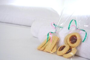 A white bed with a pillow and two packages of cookies tied with green and pink ribbons. - Locar-in Gramado Residencial Centro Bem Estar (Gramado)