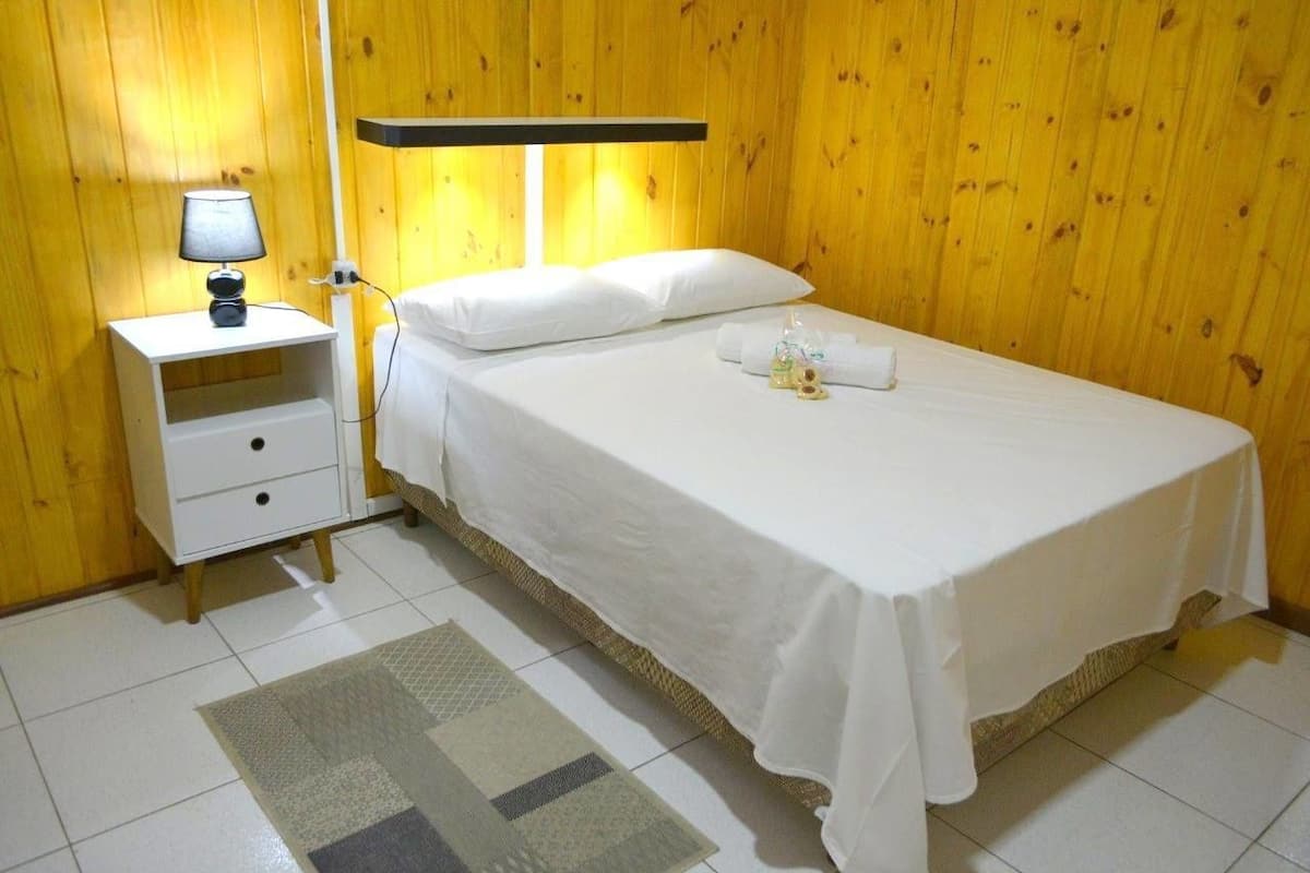 Ein ordentlich bezogenes Bett mit weißen Leinen, ein Nachttisch mit Lampe und ein kleiner Teppich auf dem Boden.