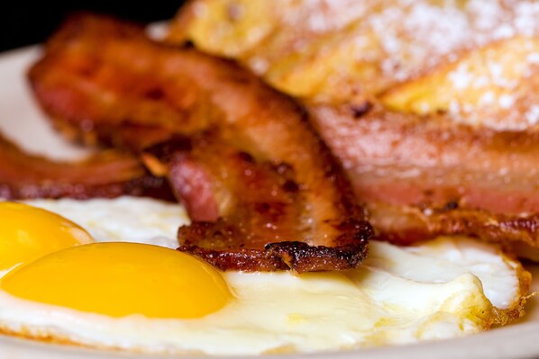 A plate with bacon, two fried eggs, and a slice of ham. - Grand Colonial B&B (Herkimer)