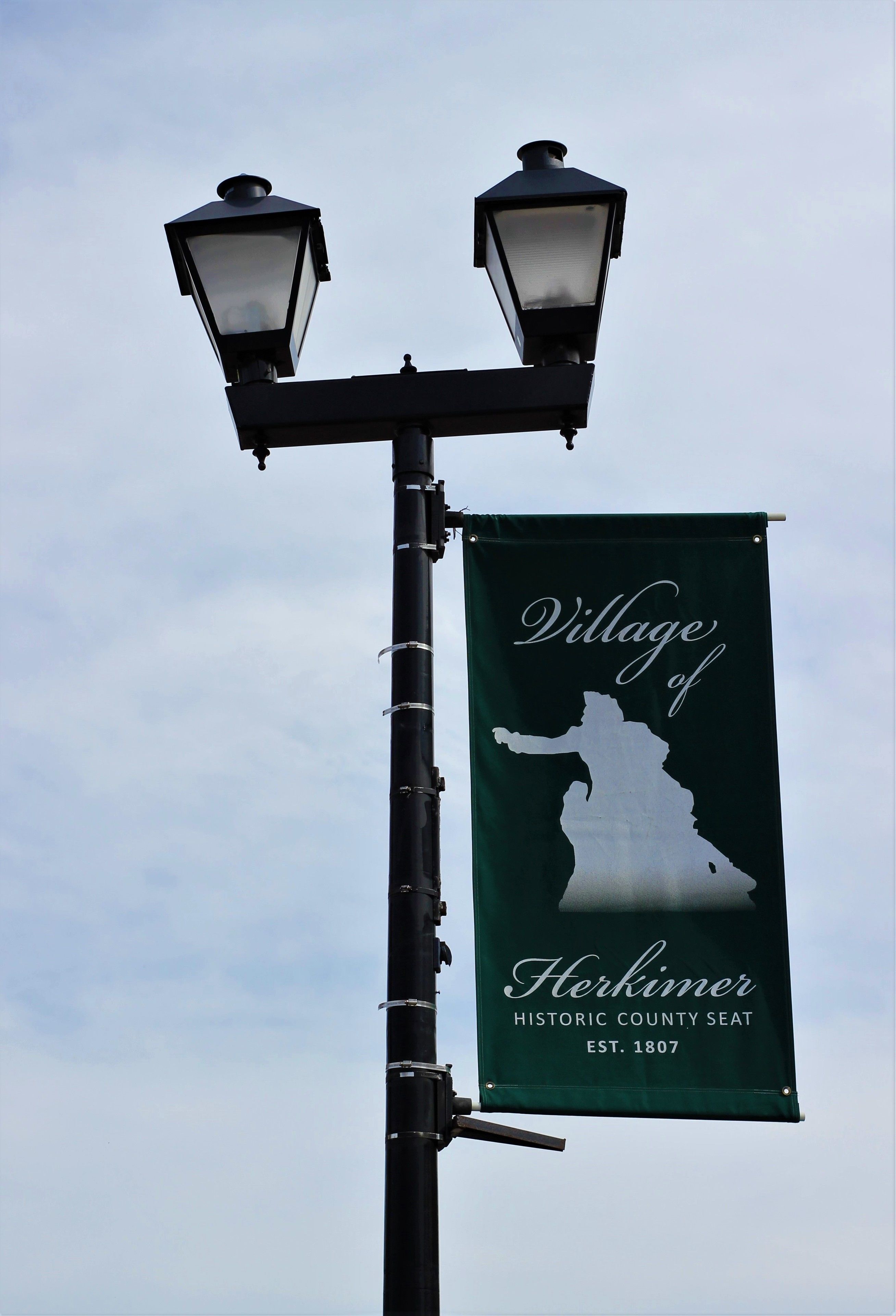 A street lamp with two lanterns and a banner for the Village of Herkimer Historic County Seat.