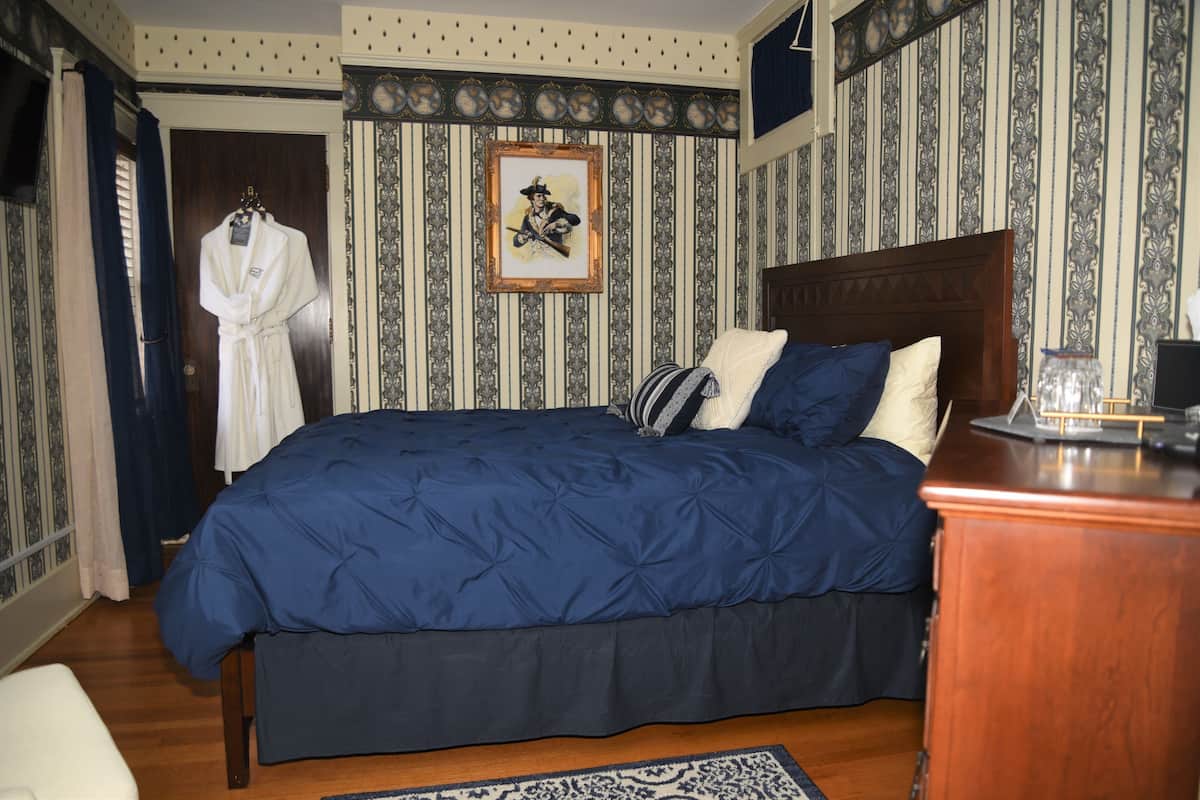 A bedroom with a large bed, a wooden headboard, a framed picture on the wall, and a robe hanging on a door.